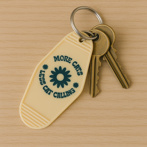 More Cats, Less Cat Calling Keychain
Equal parts protest and purr.

A retro motel-style tag with zero tolerance for street sleaze. Molded in buttercream plastic with a punch of deep green text and a bold daisy, it says what you’re thinking: MORE CATS, LESS CAT CALLING.

Clip it to your keys like brass knuckles for the modern feminist.  Fierce, unapologetic, loud, feral and decidedly not here for your unsolicited commentary.
	•	3.8” x 2” vintage motel shape
	•	Chunky molded plastic with raised lettering
	•	D