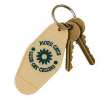Load image into Gallery viewer, More Cats, Less Cat Calling Keychain
Equal parts protest and purr.

A retro motel-style tag with zero tolerance for street sleaze. Molded in buttercream plastic with a punch of deep green text and a bold daisy, it says what you’re thinking: MORE CATS, LESS CAT CALLING.

Clip it to your keys like brass knuckles for the modern feminist.  Fierce, unapologetic, loud, feral and decidedly not here for your unsolicited commentary.
	•	3.8” x 2” vintage motel shape
	•	Chunky molded plastic with raised lettering
	•	D